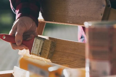 Person streicht Holz mit Pinsel